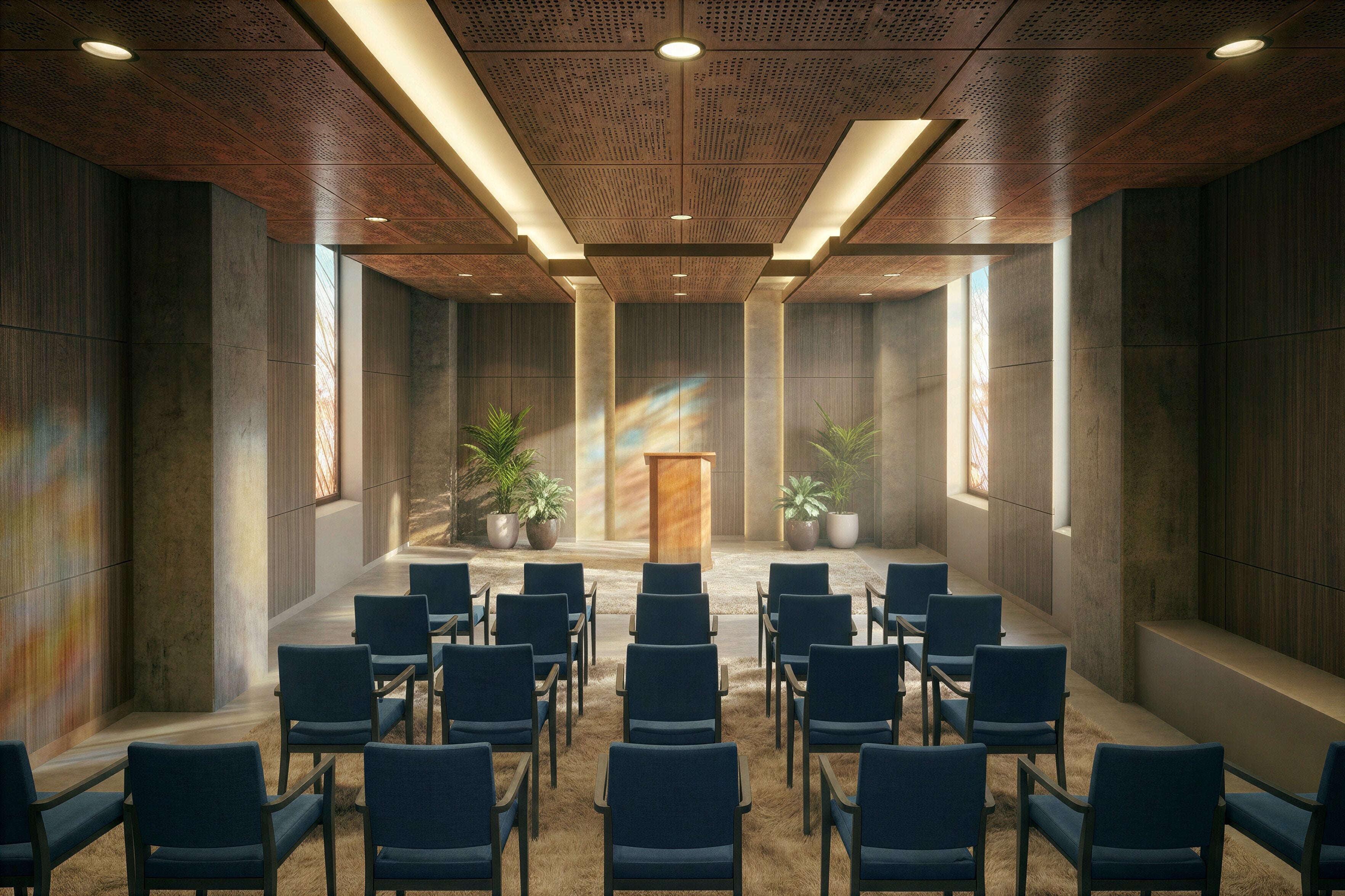 Interior view of the non‑denominational chapel at Austin State Hospital designed with architecture+, showing rows of blue cushioned chairs oriented toward a wooden podium framed by tall textured walls and controlled natural daylight. Warm wood ceiling panels, recessed lighting, and potted greenery create a serene, human‑scaled environment that supports emotional respite and quiet reflection within a behavioral health setting.