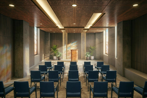 Interior view of the non‑denominational chapel at Austin State Hospital designed with architecture+, showing rows of blue cushioned chairs oriented toward a wooden podium framed by tall textured walls and controlled natural daylight. Warm wood ceiling panels, recessed lighting, and potted greenery create a serene, human‑scaled environment that supports emotional respite and quiet reflection within a behavioral health setting.