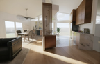 Interior view of the Niskayuna kitchen renovation showing a contemporary interpretation of Mid‑Century design, with warm wood cabinetry, a marble countertop, and clean modern lines. The open dining area includes a wooden table, upholstered chairs, and a sculptural pendant light. Large windows bring in natural light, while a vertical slat partition and curated artwork reinforce the project’s refined material palette and architectural authenticity.