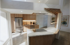 Interior view of the Niskayuna kitchen renovation showing a contemporary take on Mid‑Century design. The space features light wood cabinetry, a marble island with an integrated cooktop, and pendant lights suspended from a slatted wood ceiling detail. Modern appliances, clean lines, and a refined material palette create a warm, functional anchor that bridges the home’s original character with an updated, livable aesthetic.