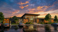 Exterior view of the Family Counseling Center designed with architecture+, showing a welcoming modern façade with tall glass panels, warm wood beams, and a clearly defined central entry. The building sits within landscaped greenery and is captured at sunset, with soft light reflecting across the wet pavement. The design emphasizes openness, safety, and human‑centered care through its transparent, approachable architectural expression.