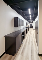Rear perspective of Alchemy Studios and Salon in Cohoes, NY, showing a minimalist corridor with dark cabinetry, a black countertop, exposed ceiling elements, and linear LED lighting. The clean material palette and controlled illumination reflect the studio’s design focus on light, openness, and refined spatial transitions.
