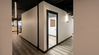 Architectural interior view of Alchemy Studios and Salon in Cohoes, NY, showing a minimalist corridor with light walls, wood-patterned flooring, and a glass door framed in dark trim. The exposed black ceiling with linear lighting and visible piping reinforces the studio’s contemporary, gallery-like aesthetic focused on light, clarity, and refined spatial transitions.